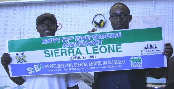 Abdul and Alex from Sierra Leone Brighton Association, holding up a paper banner advertising their independence day event.